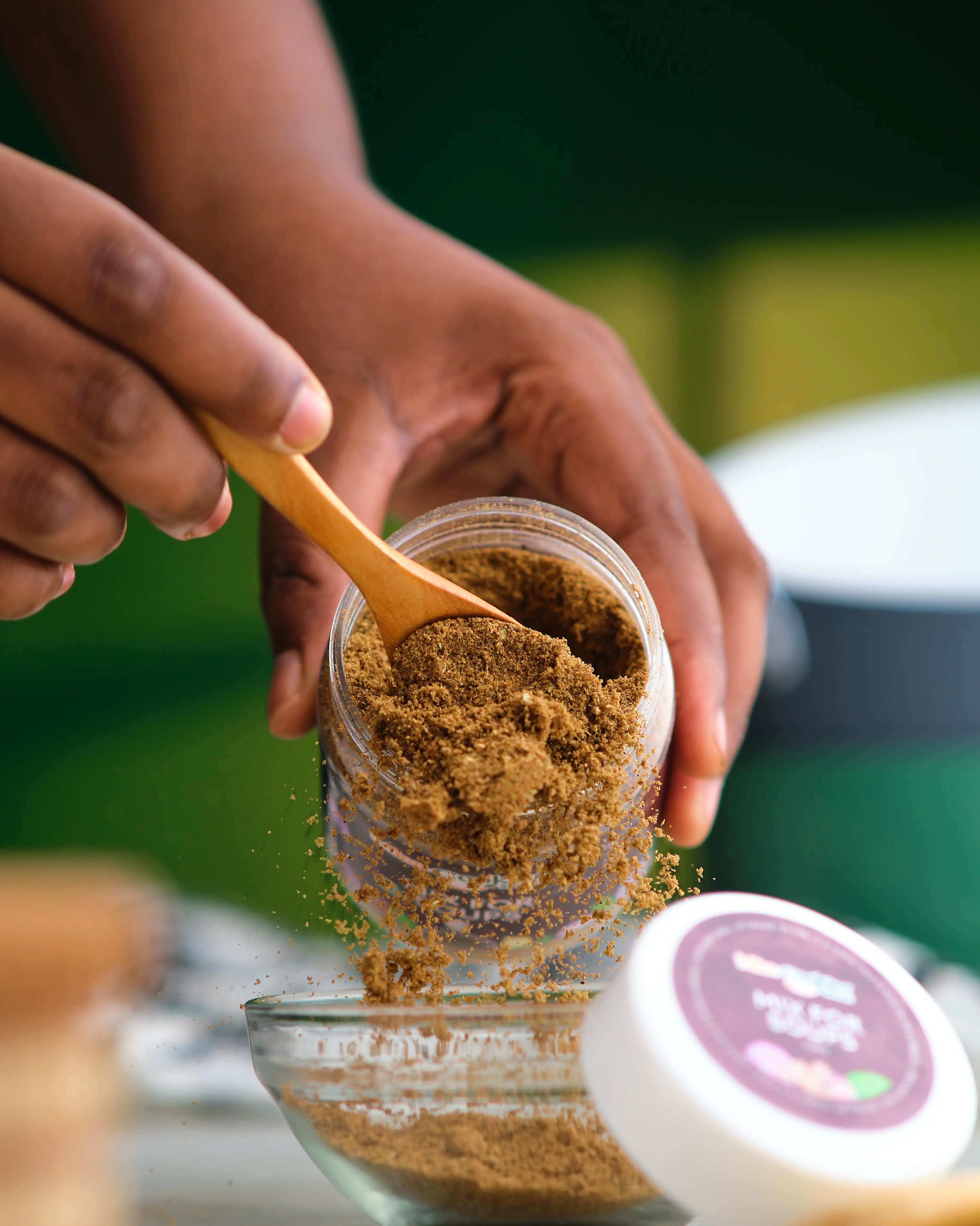 Hands pouring ground spice from a jar into a glass bowl outdoors