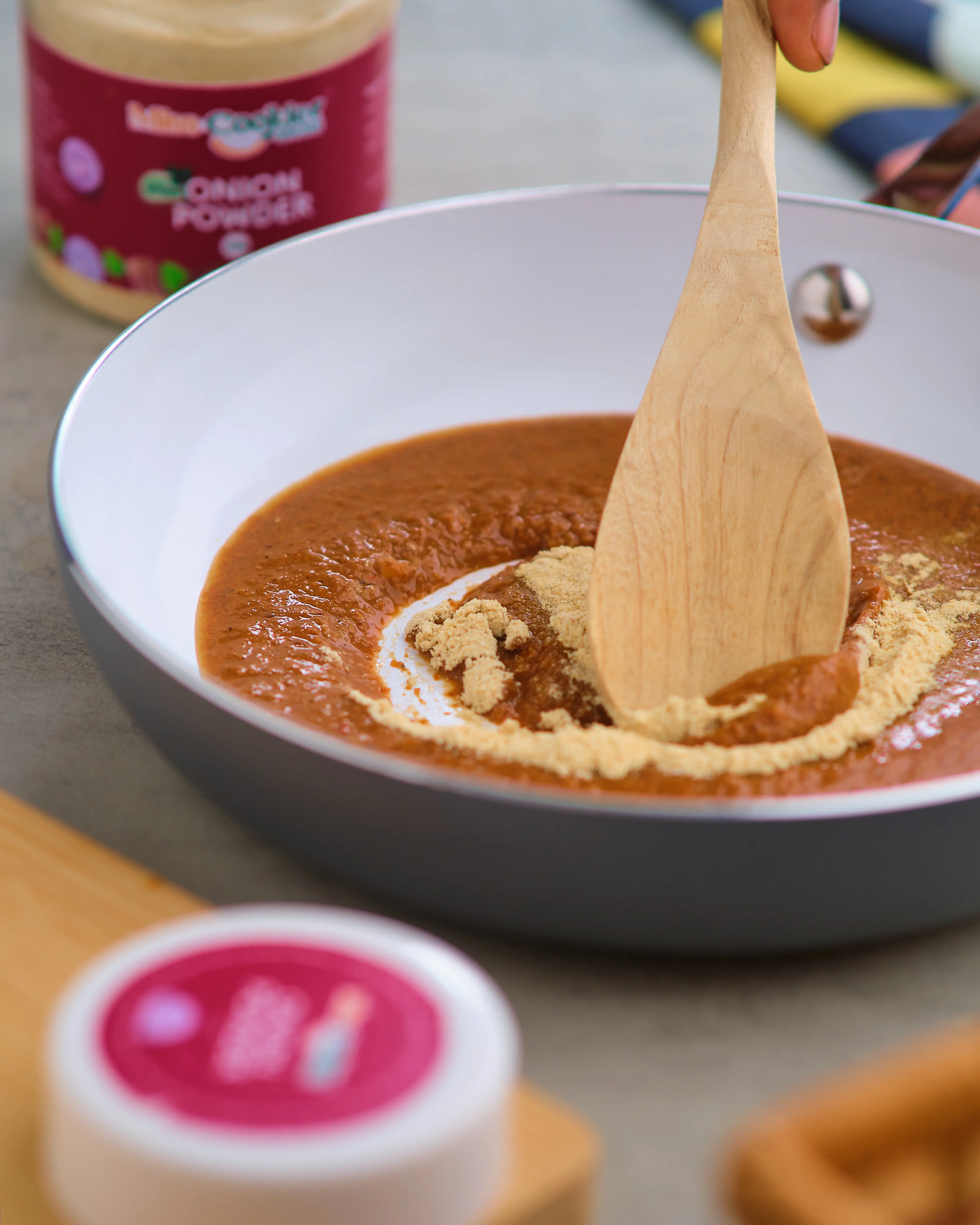 Wooden spoon stirring onion powder into tomato sauce in a pan