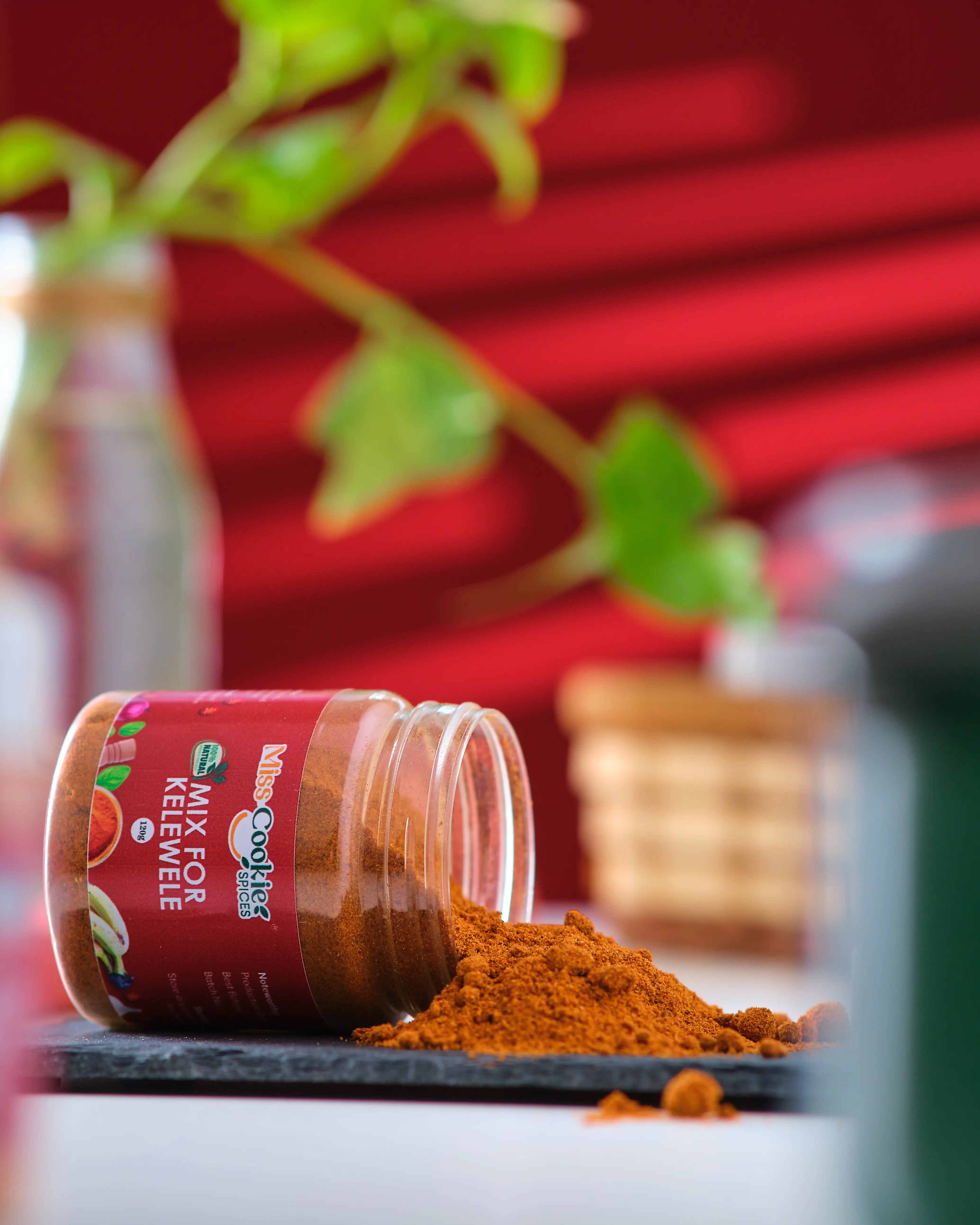 Open jar of Miss Cookie Mix for Kelewele spilled onto a surface beside a plant
